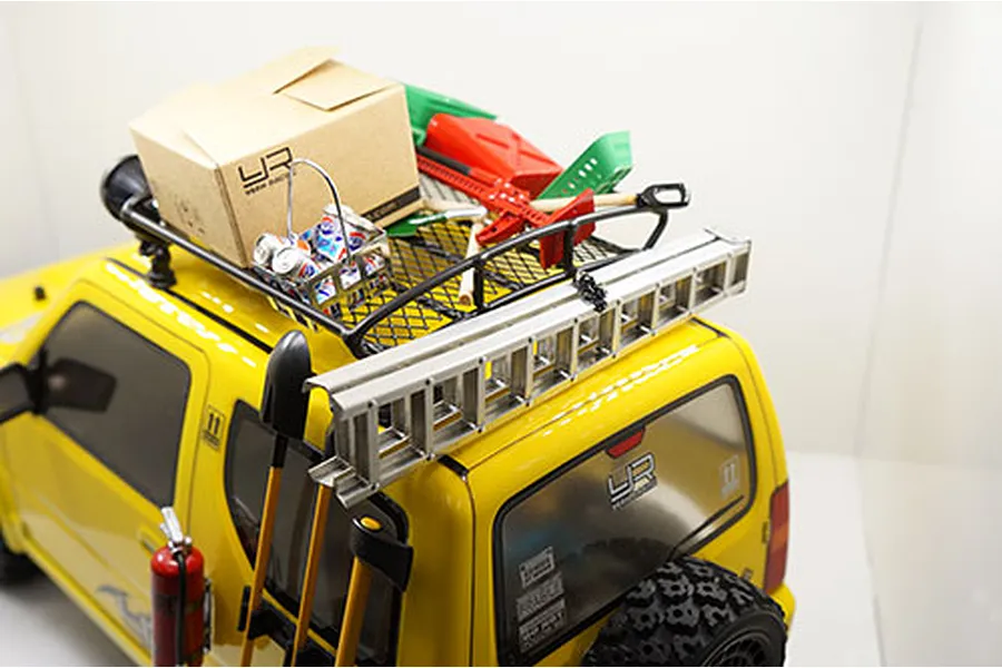 A silver aluminium scale ladder mounted on the roof rack of a yellow RC crawler vehicle.