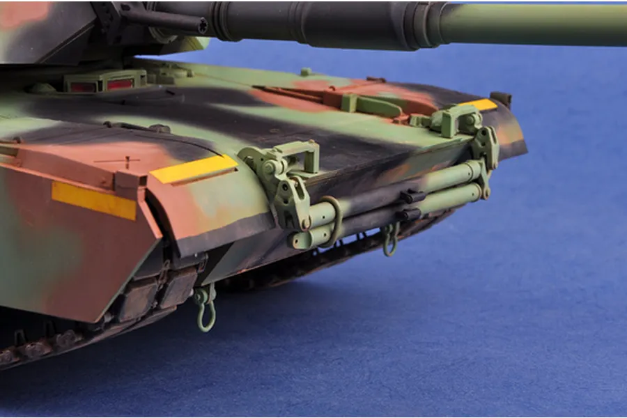 Close-up of the front hull and turret of a camouflaged M1 Abrams scale model tank, showing detailed weathering and tow cable mounts.