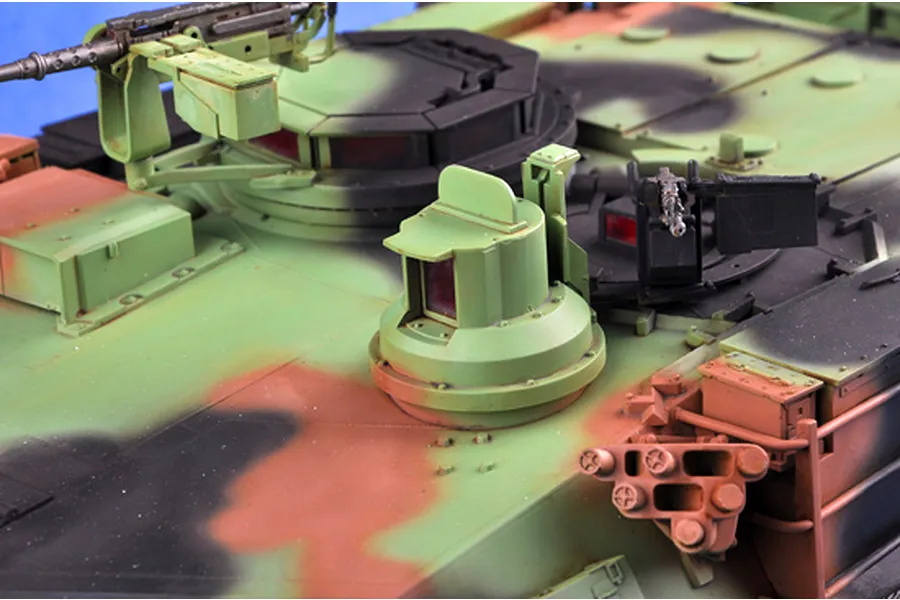 Close-up of the turret top of a 1/16 scale M1A1 Abrams model tank featuring camouflage paint, machine guns, and hatches.