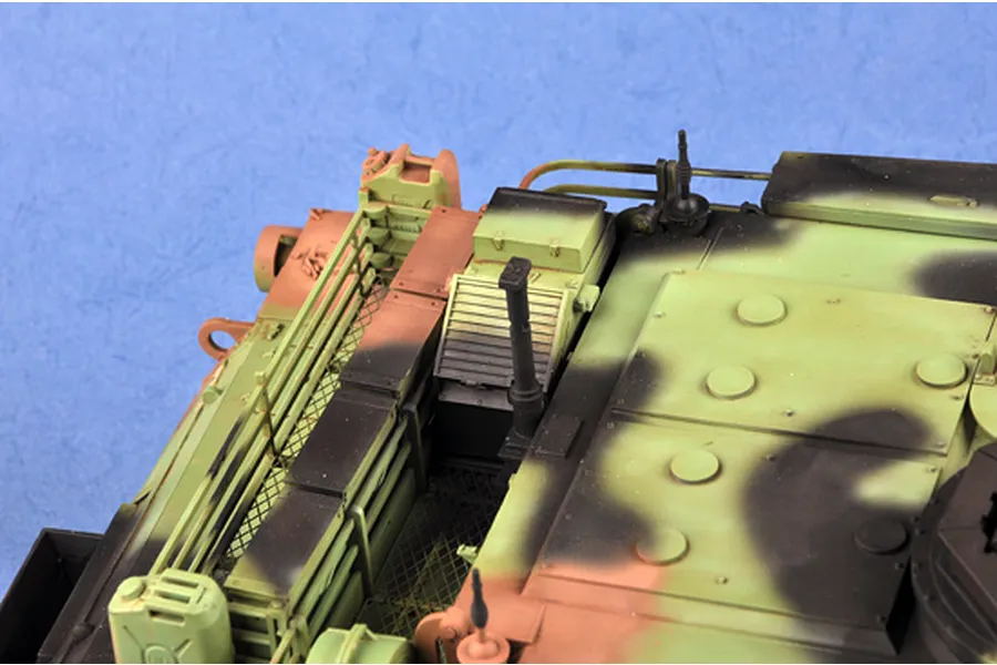 Close-up of the rear deck of a camouflaged M1A1 Abrams tank model, showing engine vents, storage racks, and antennas.