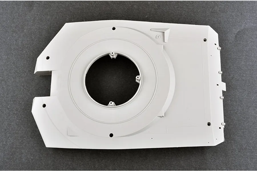 A light grey plastic model tank turret base part from a 1/16 scale Trumpeter Abrams kit, viewed from above against a dark grey background.