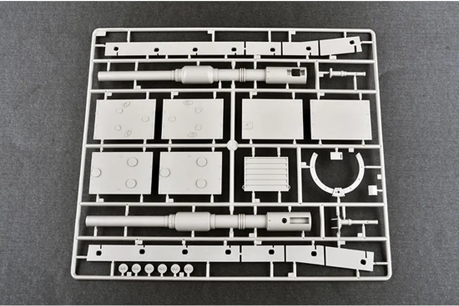 A grey plastic model kit sprue containing tank parts, including two large gun barrels and various flat armor panels, set against a dark grey background.