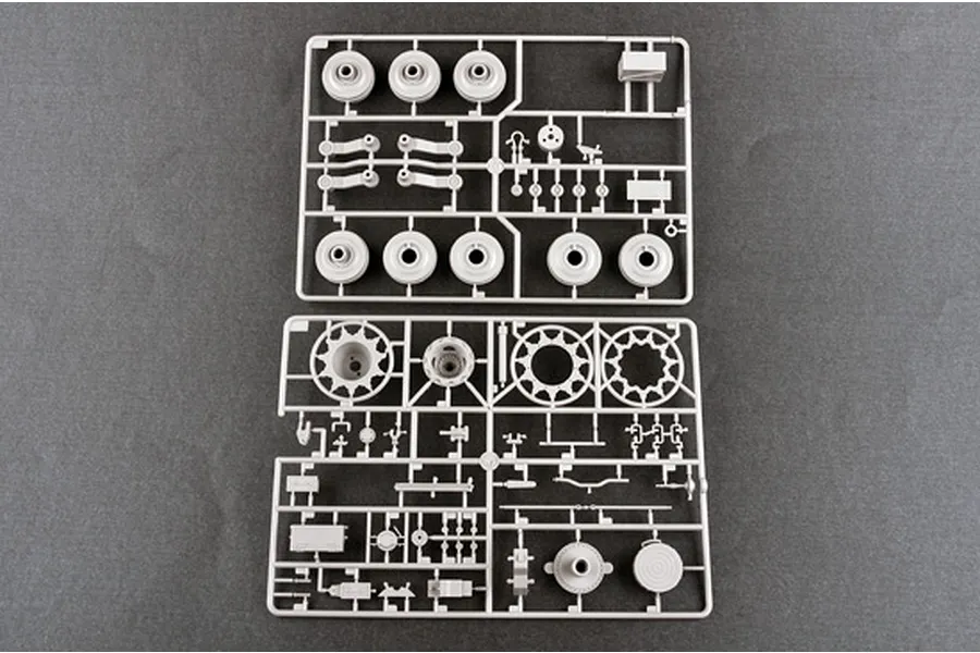 Two grey plastic model kit sprues containing tank road wheels, drive sprockets, and suspension components on a dark grey background.