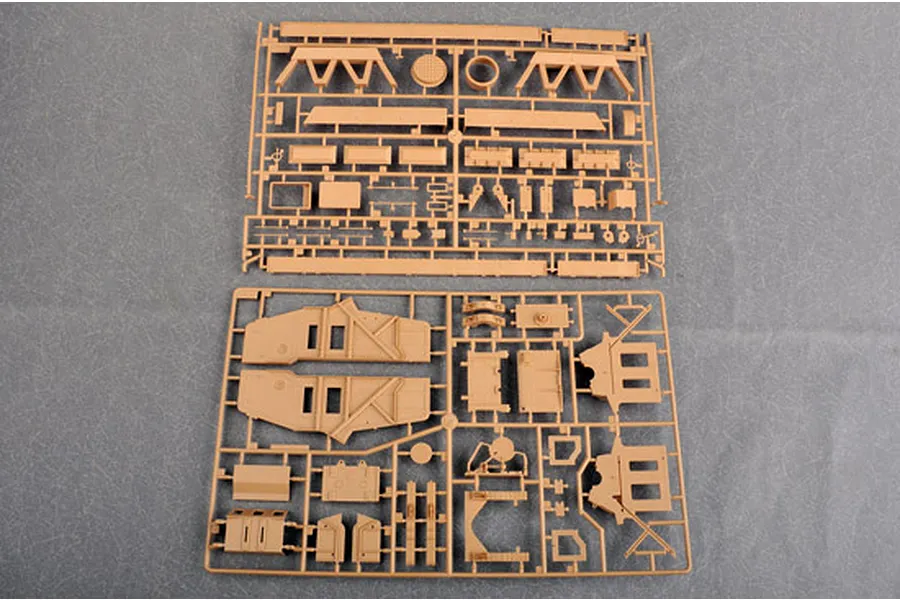 Two tan plastic model kit sprues containing various vehicle parts laid out on a grey surface.