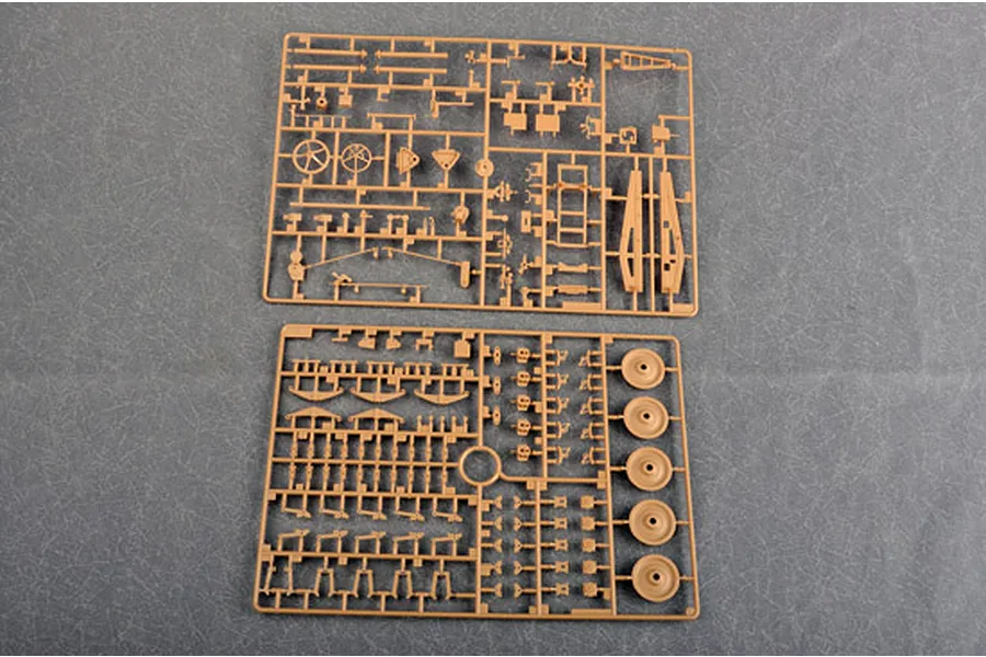 Two tan plastic model kit sprues containing various small parts for a military vehicle model, laid out on a grey surface.