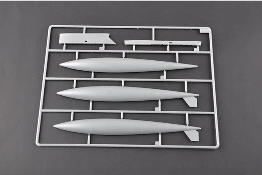 A grey plastic sprue from a model kit containing three external fuel tanks and two flat structural components.
