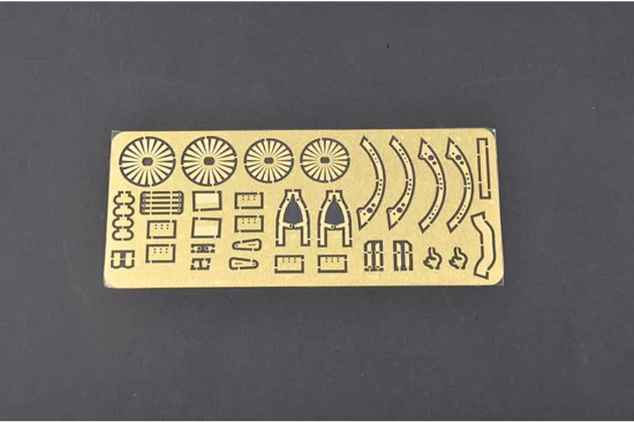 A photo-etched brass detail sheet for a model kit, featuring various small parts like fan blades and structural components on a dark grey background.