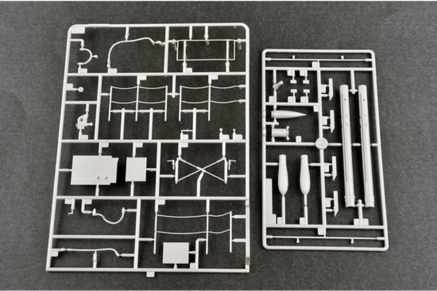 Two grey plastic model kit sprues containing various small parts, including cylindrical tubes and flat panels, laid out on a dark grey surface.