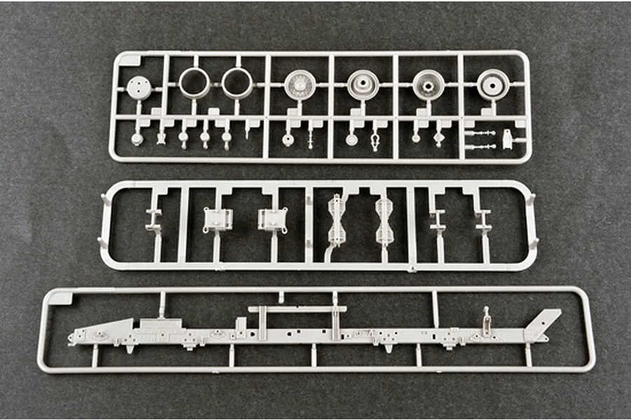 Three grey plastic model kit sprues containing various vehicle parts laid out on a dark grey surface.