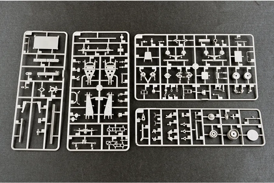 Four grey plastic model kit sprues containing various vehicle parts laid out on a dark surface.