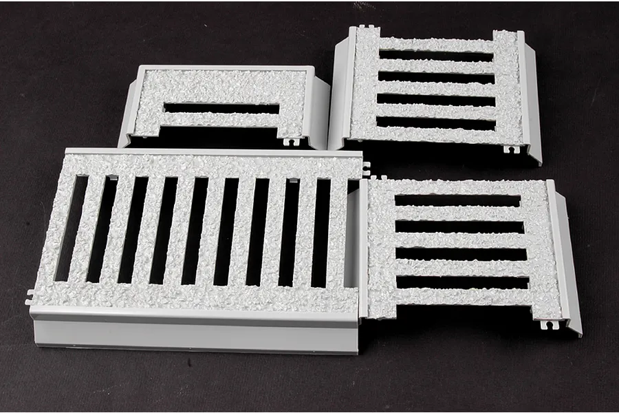 Four grey plastic model kit parts with textured surfaces, likely representing locomotive or vehicle grilles, arranged on a black background.