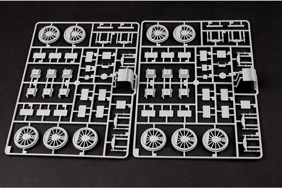 Two identical grey plastic model kit sprues containing train wheels and various small mechanical parts on a black background.