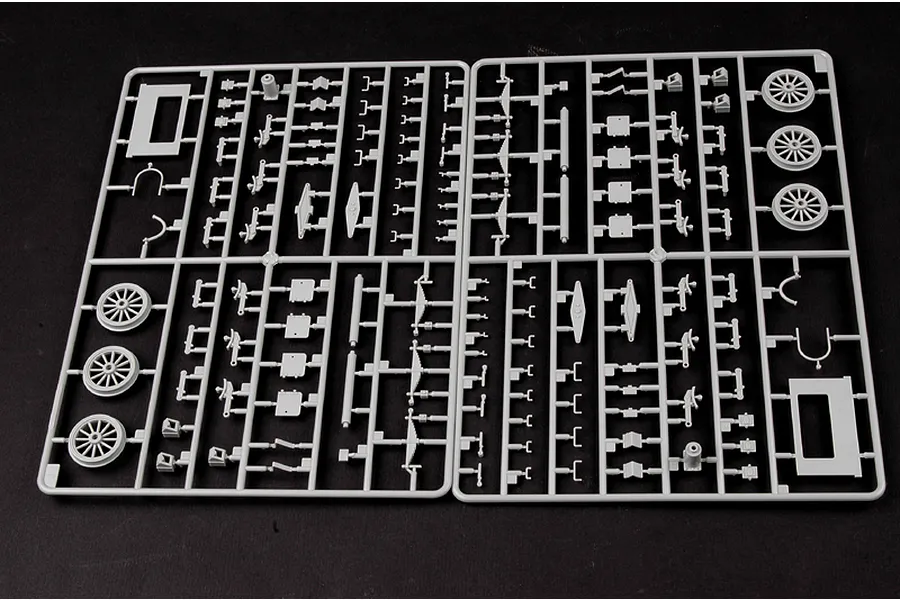 Two grey plastic model kit sprues containing various small parts and six train wheels on a black background.