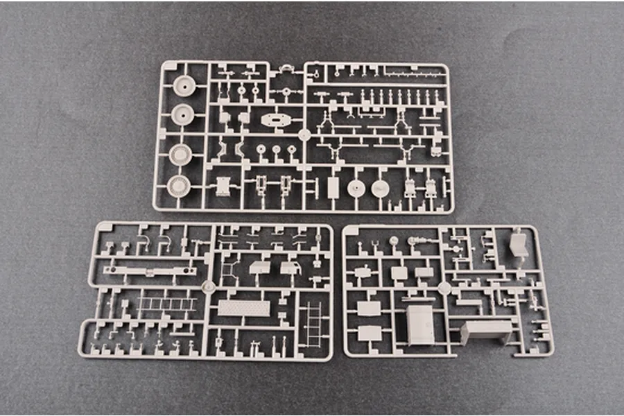 Three grey plastic model kit sprues containing various vehicle parts laid out on a dark grey surface.