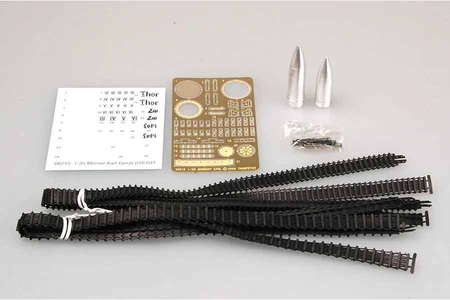 Components for a 1/35 scale Trumpeter Morser Karl model kit, including decals, a photo-etched brass sheet, two metal shells, and black plastic tank tracks.
