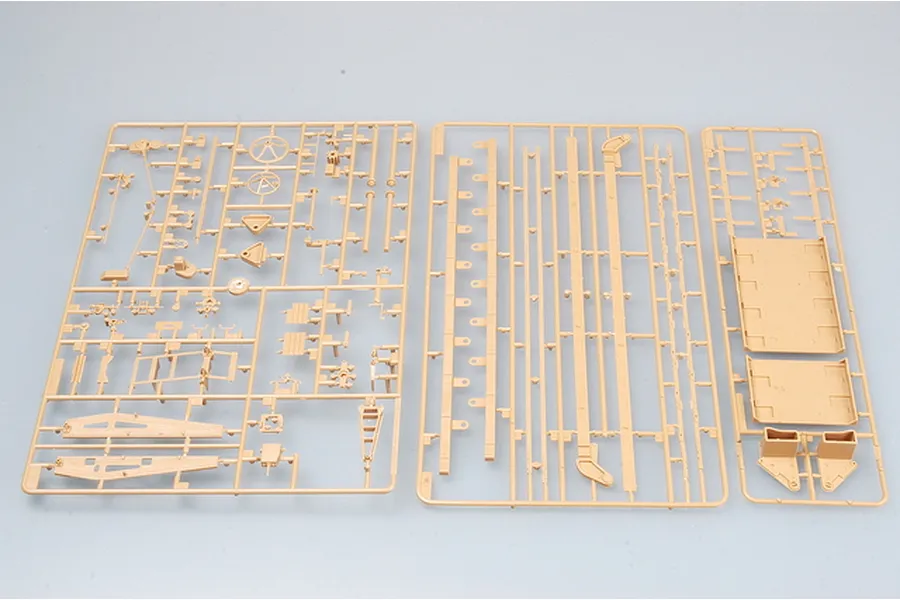 Three tan plastic model kit sprues containing various parts for a military vehicle model, laid out on a light grey background.