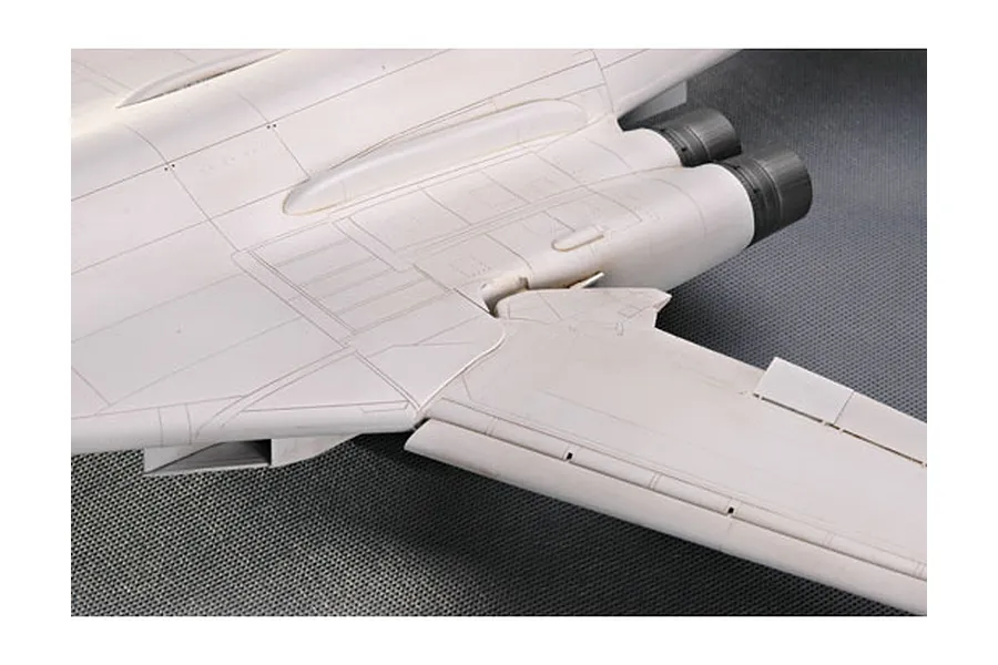 Close-up of the rear fuselage and wing section of an unpainted plastic model aircraft kit, showing detailed panel lines and engine exhaust nozzles.