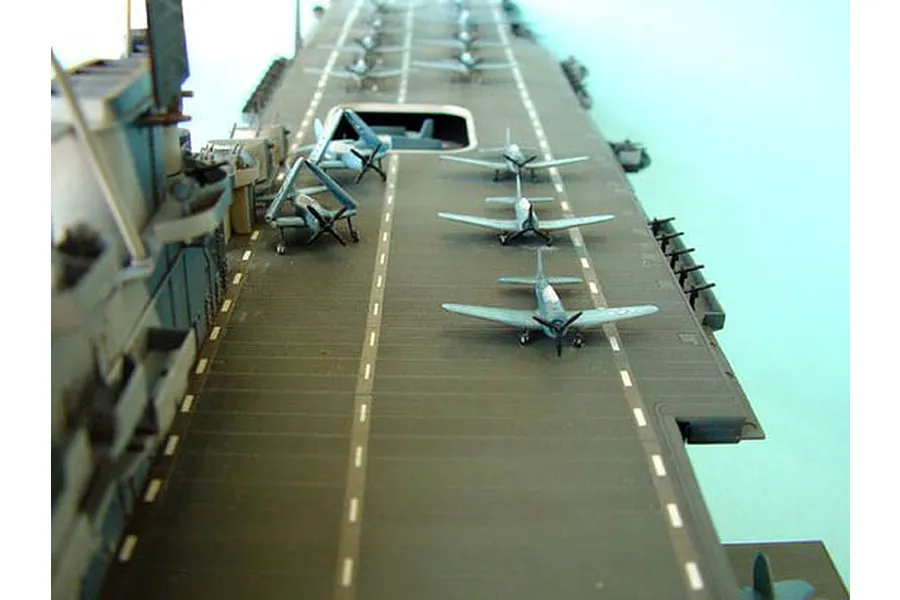 A high-angle view of a 1/350 scale model aircraft carrier deck with several small model airplanes parked on the flight deck.