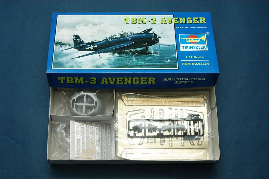 Open box of Trumpeter 1/32 scale TBM-3 Avenger plastic model kit showing box art, photo-etched parts, and plastic components.
