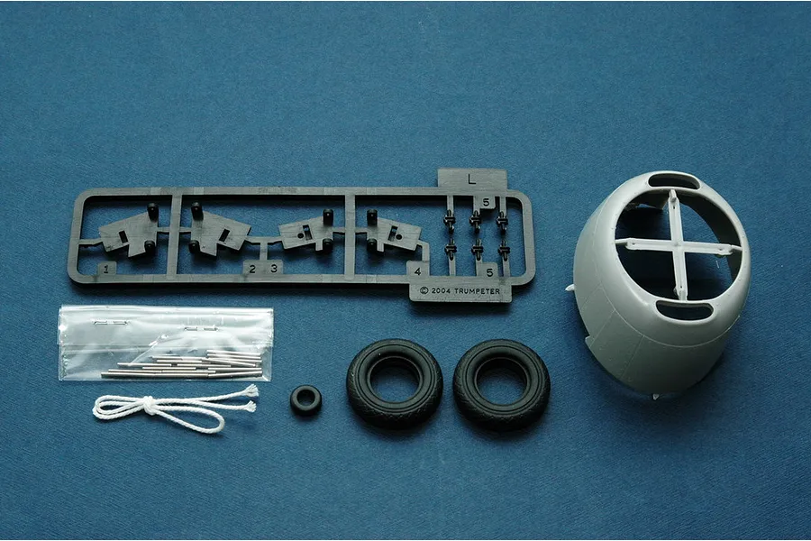 Plastic model kit parts for a Trumpeter 1/32 TBM-3 Avenger, including a sprue, engine cowling, rubber tires, metal pins, and string on a blue background.
