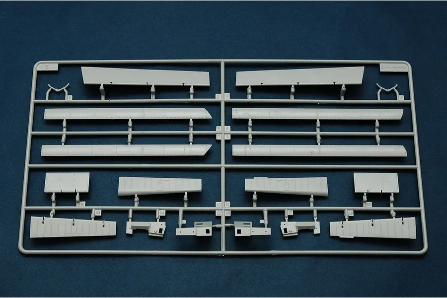 A grey plastic model kit sprue containing various aircraft wing and control surface components on a dark blue background.