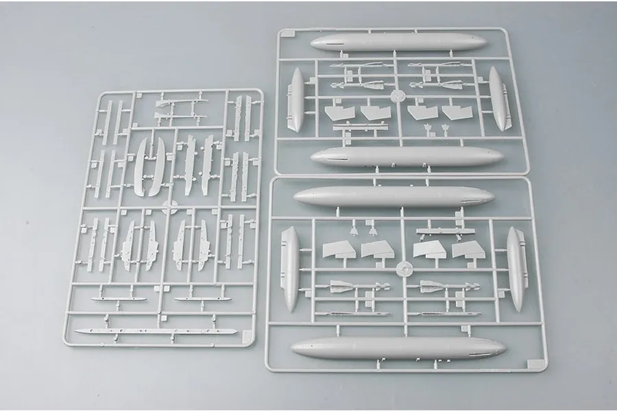 Three grey plastic model kit sprues containing aircraft parts and external fuel tanks on a plain background.