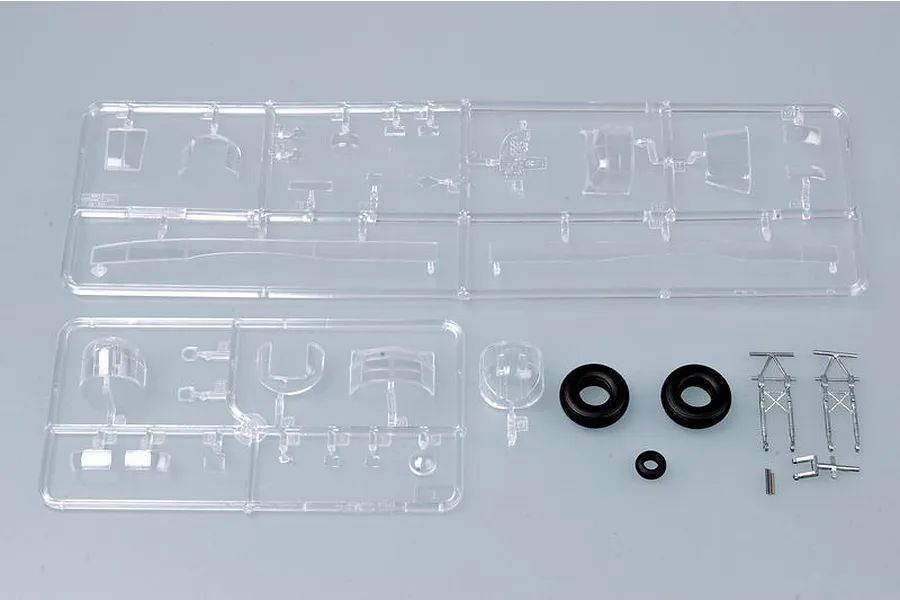 Clear plastic model kit sprues containing aircraft canopy parts, two rubber tires, and small metal landing gear components on a grey background.