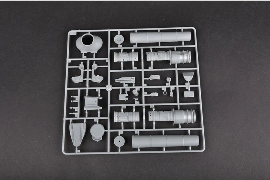 A grey plastic sprue containing various model aircraft parts, including engine components and cylindrical sections, on a dark background.