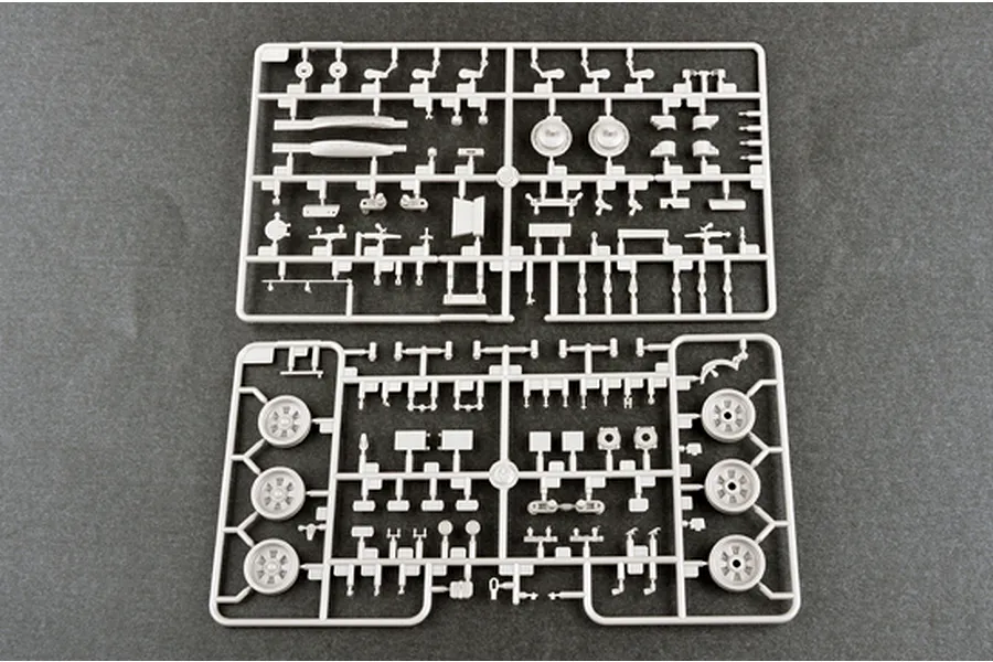 Two grey plastic model kit sprues containing various tank parts, including wheels and suspension components, laid out on a dark grey surface.