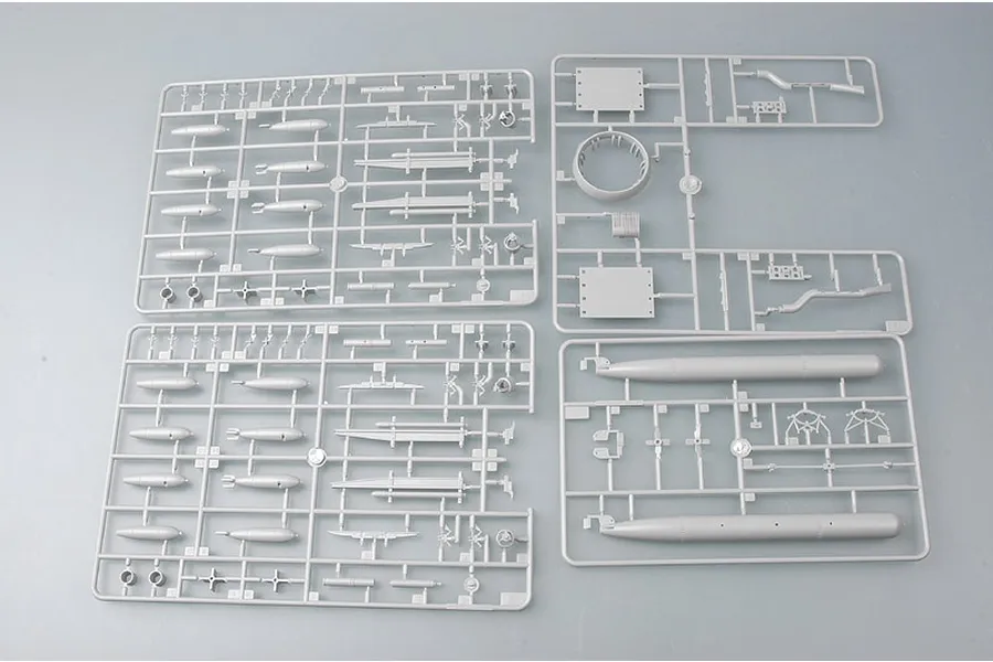 Four grey plastic model kit sprues containing various aircraft parts, including bombs and fuselage components, laid out on a plain surface.