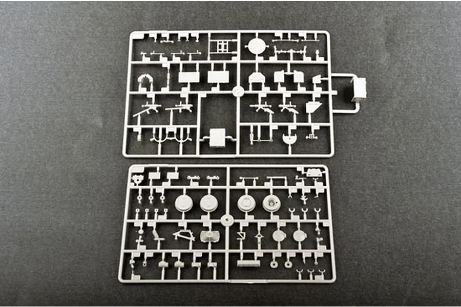 Two grey plastic model kit sprues containing various vehicle parts for a 1/35 scale military model kit, laid out on a dark grey surface.