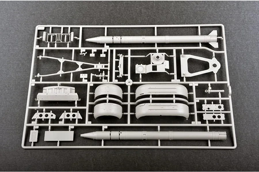A grey plastic sprue containing various model kit parts, including two missile bodies and vehicle components, on a dark grey background.