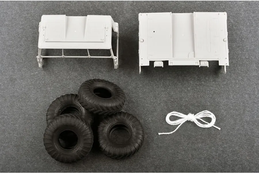 Unassembled plastic model kit parts including truck cab roof, chassis section, four rubber tires, and a length of white string on a grey surface.