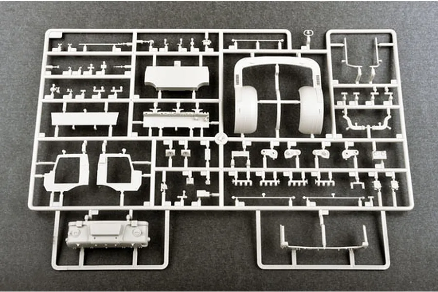 A grey plastic sprue containing various unpainted model kit parts for a military vehicle, laid out on a dark grey surface.