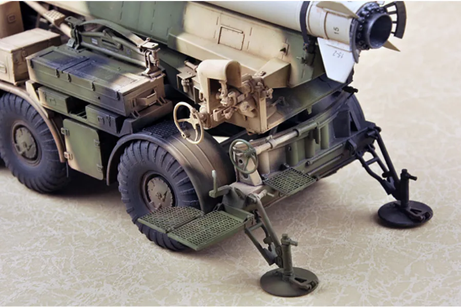 A detailed scale model of a Russian 9P113 TEL military truck with a Luna-M missile, showing rear stabilizers, storage boxes, and camouflage paint.