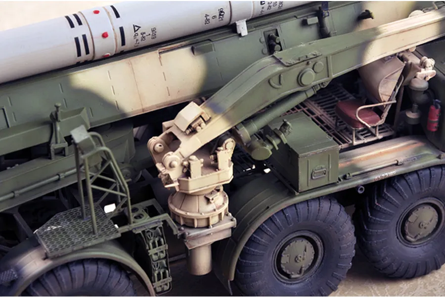 A detailed close-up of a 1/35 scale model of a Russian 9P113 TEL military vehicle, showing the missile launcher mechanism, tires, and painted camouflage finish.