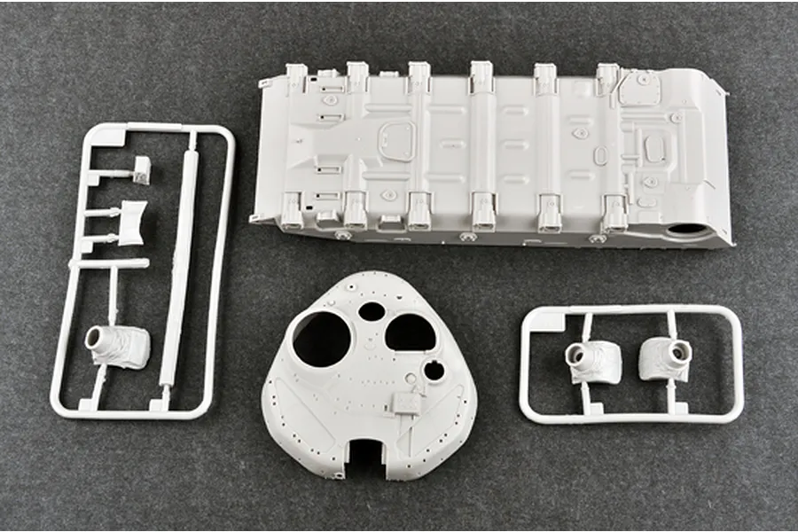 Unassembled plastic model tank parts including the hull, turret, and sprue frames on a dark grey surface.