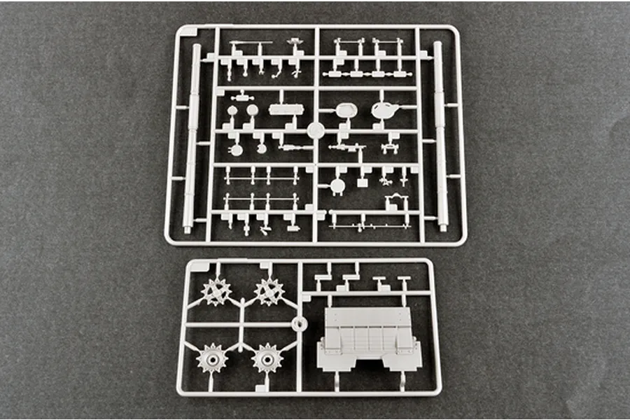 Two grey plastic model kit sprues containing various tank parts, including sprockets and hull sections, laid out on a dark grey surface.
