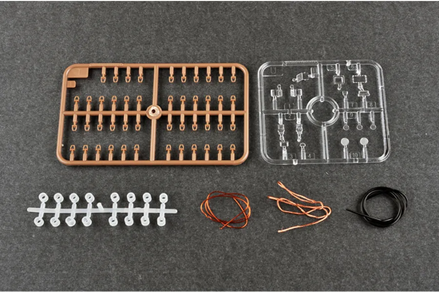 Plastic model kit parts including brown and clear sprues, small white plastic parts, copper wire, and black tubing on a grey surface.