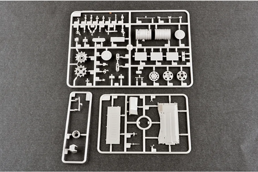 Three grey plastic model kit sprues containing various tank parts laid out on a dark grey surface.