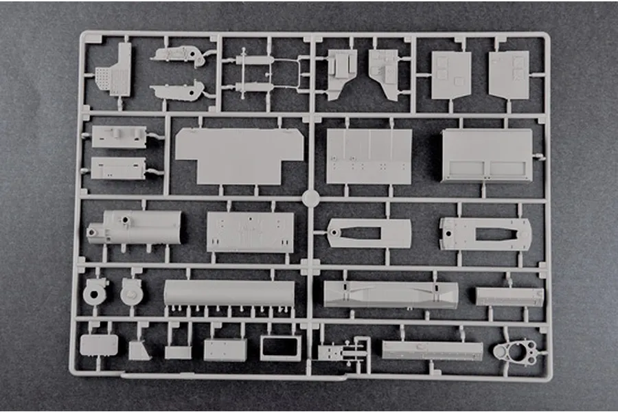 A grey plastic sprue containing various unpainted model kit parts for a military vehicle, set against a dark grey background.