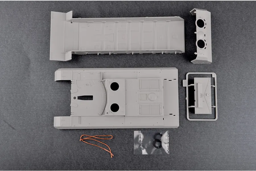 Top-down view of unpainted grey plastic model kit parts for a 1/35 scale Soviet 2S7m self-propelled gun, including hull sections and small accessories.