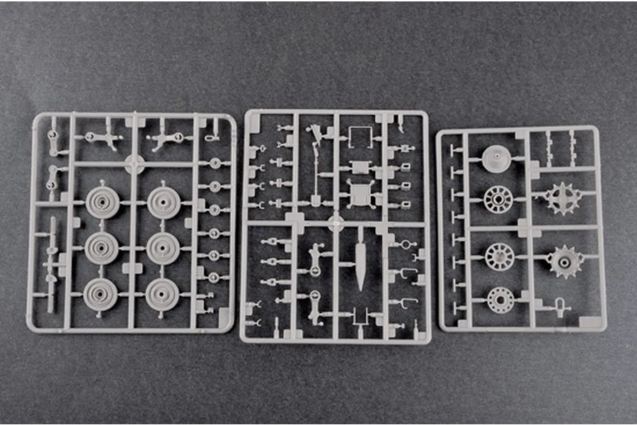 Three grey plastic model kit sprues containing various vehicle parts like wheels and suspension components on a dark grey background.