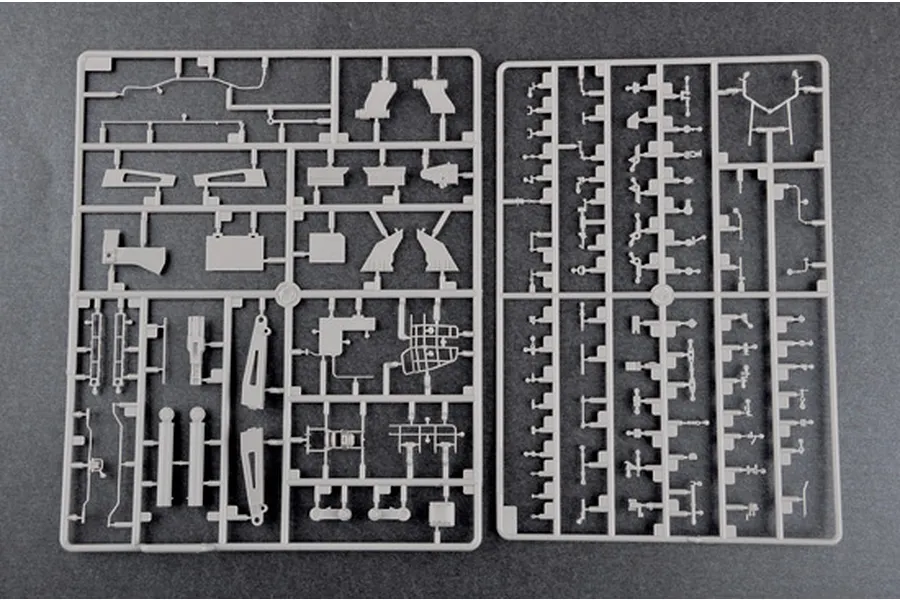 Two grey plastic model kit sprues containing various small parts for a 1/35 scale military vehicle model, laid out on a dark grey surface.