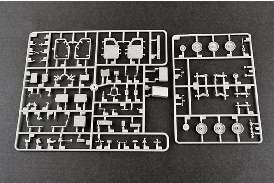 Two grey plastic model kit sprues containing various vehicle parts, including doors, wheels, and suspension components, laid out on a dark surface.