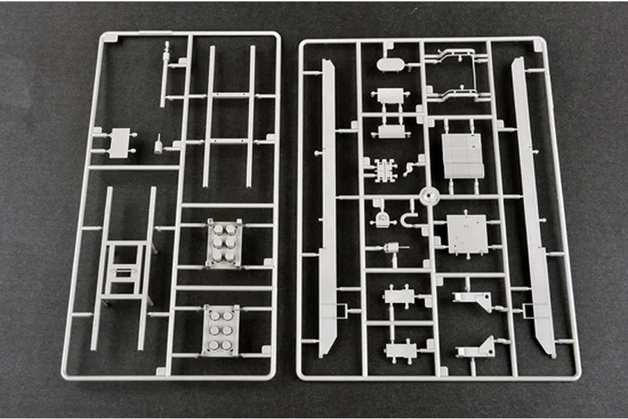 Two grey plastic model kit sprues containing various vehicle parts laid out on a dark grey surface.