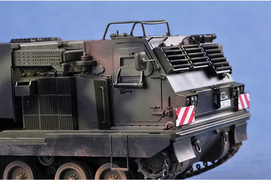 A detailed scale model of a military Mobile Artillery Rocket System (MARS) vehicle painted in camouflage green against a blue background.