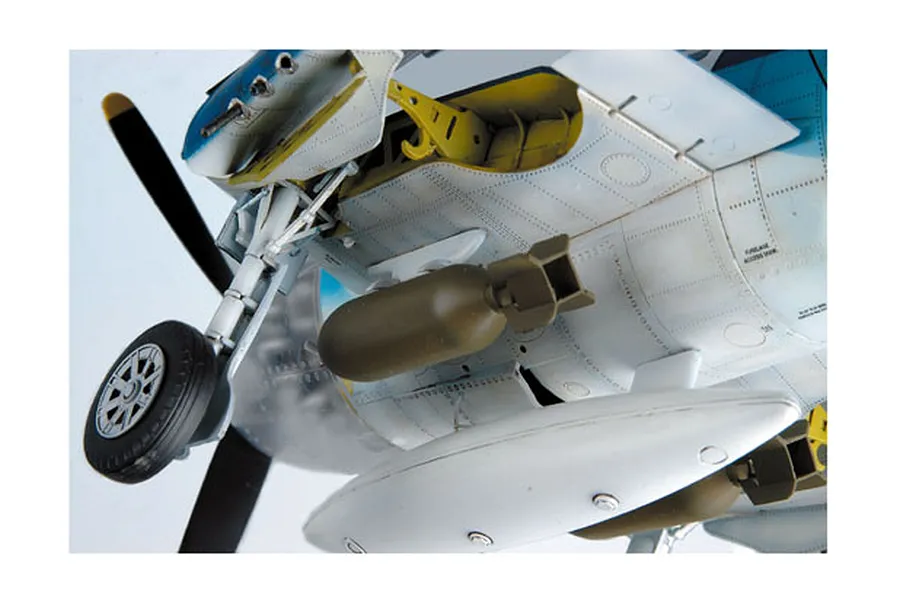 Close-up of the underside of a 1/32 scale F6F Hellcat model aircraft showing landing gear, bomb payload, and detailed panel lines.