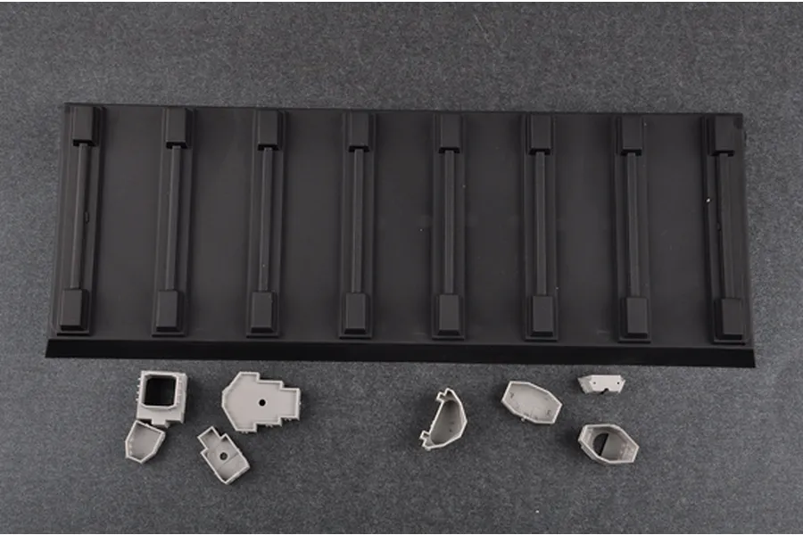 A black plastic display stand for a model ship alongside several small grey plastic model components on a dark grey surface.
