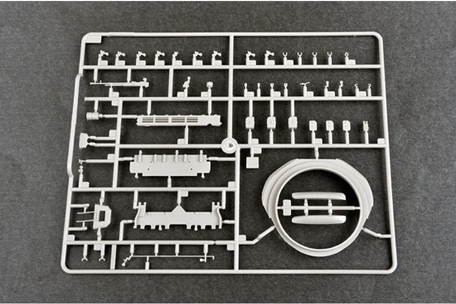 A grey plastic sprue containing various unpainted model tank parts, including a turret ring and small mechanical components, on a dark grey background.